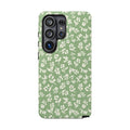 Little Things Samsung Galaxy phone case featuring tiny ivory wildflowers and delicate botanical sprigs scattered across a soft sage green background.