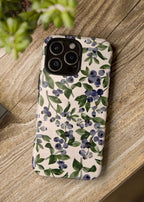 Phone case with floral design on a wooden surface next to a camera