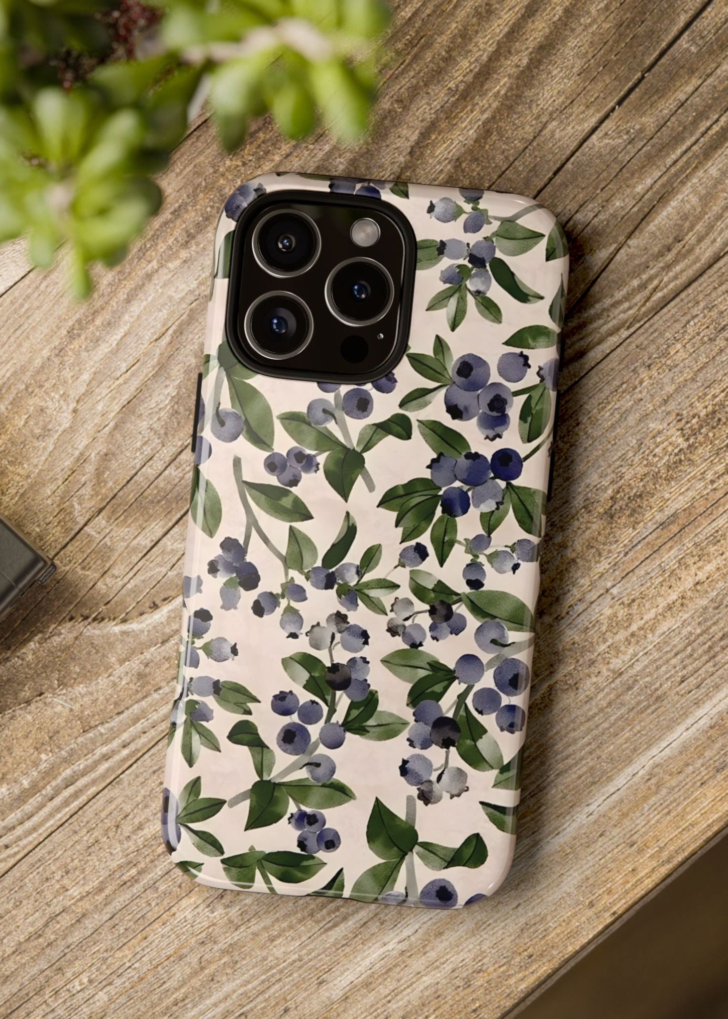Phone case with floral design on a wooden surface next to a camera