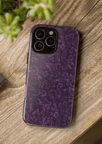 Purple floral patterned phone case on a wooden surface with a camera and plant in the background.