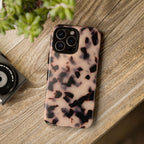 Phone case with tortoiseshell pattern on a wooden surface next to a camera and plant.