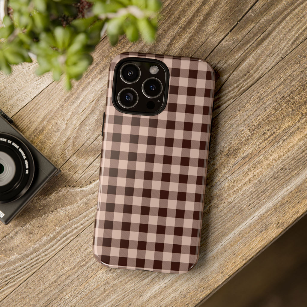 Phone case with a checkered pattern on a wooden surface next to a camera and plant.