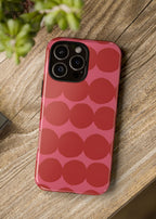 Red polka dot phone case on a wooden surface with a camera and plant in the background