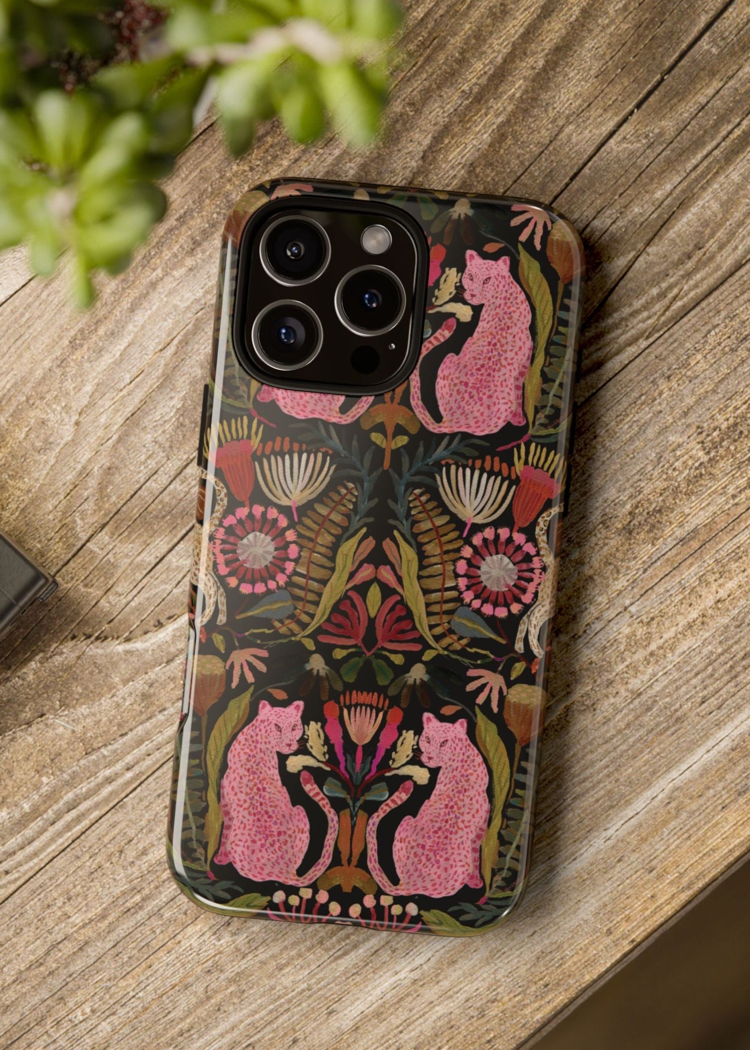 Phone case with floral and cat design on a wooden surface next to a camera