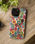 Colorful circular patterned phone case on a wooden surface with a camera and plant in the background.