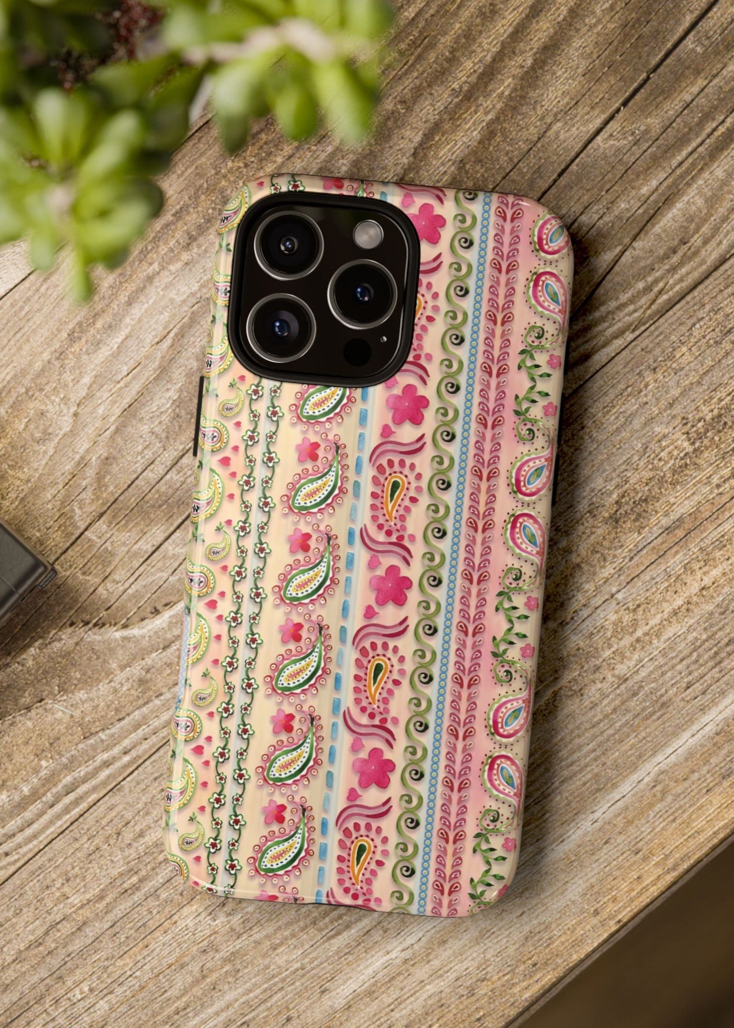 Phone case with paisley pattern on a wooden surface next to a camera and plant