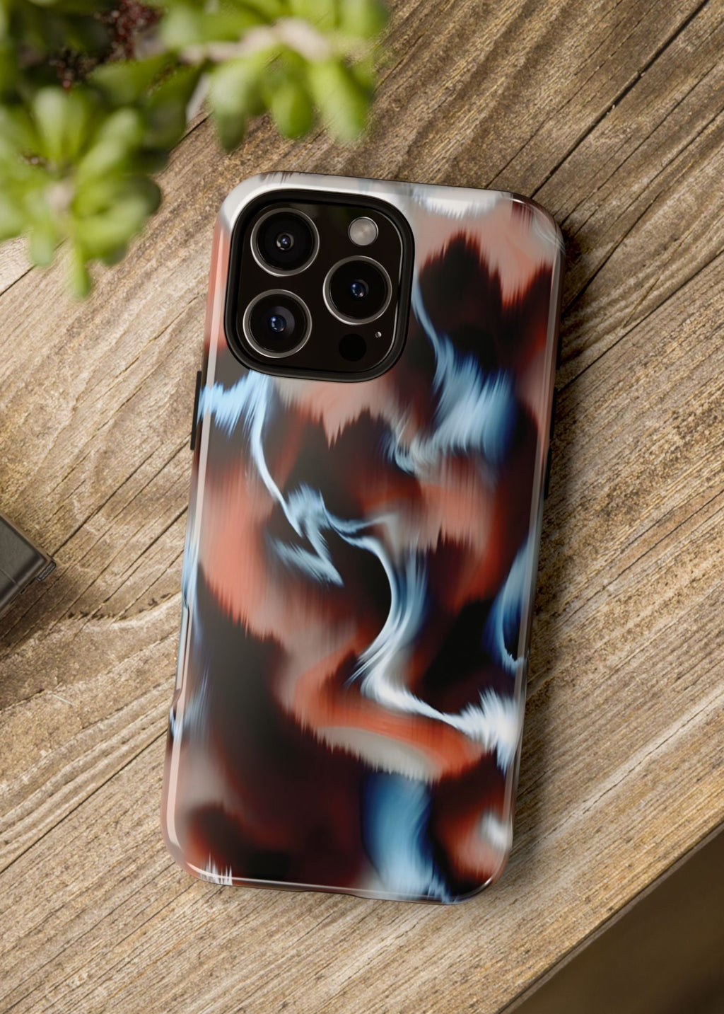 Phone case with a colorful abstract design on a wooden surface next to a camera and plant.