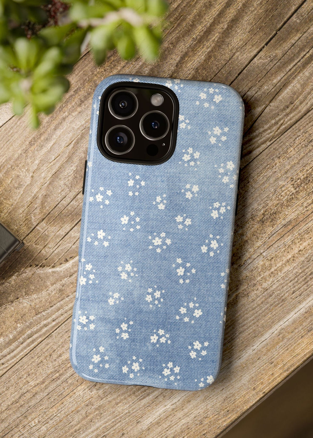 Phone case with blue floral pattern on a wooden surface next to a camera and plant.