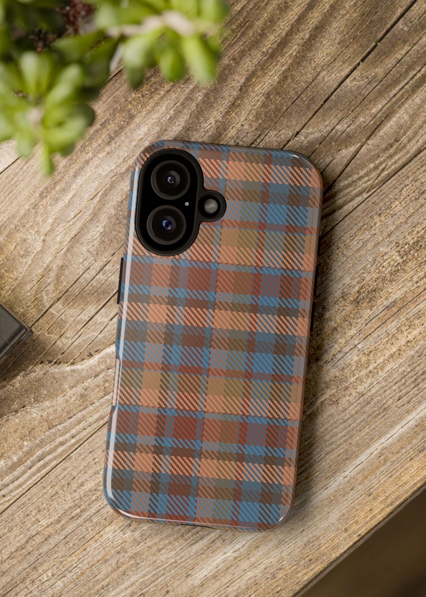 Phone case with plaid pattern on a wooden surface next to a camera